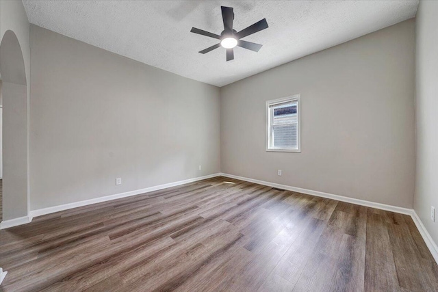 unfurnished room with a ceiling fan, wood finished floors, arched walkways, and baseboards