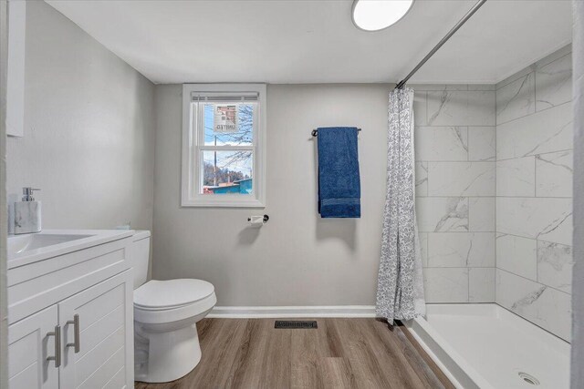 bathroom featuring visible vents, baseboards, toilet, a tile shower, and wood finished floors