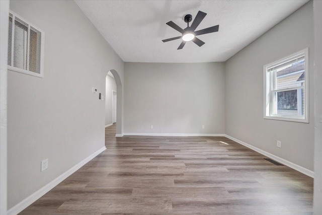 unfurnished room featuring arched walkways, visible vents, baseboards, and wood finished floors