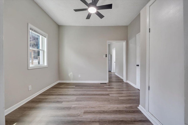 empty room with a ceiling fan, wood finished floors, baseboards, and a textured ceiling