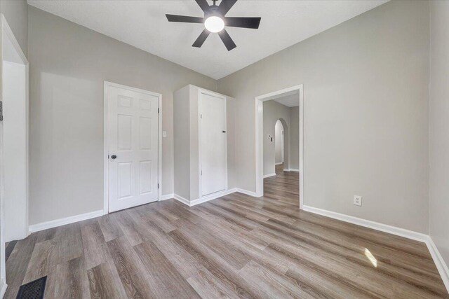 unfurnished bedroom featuring arched walkways, visible vents, baseboards, and wood finished floors