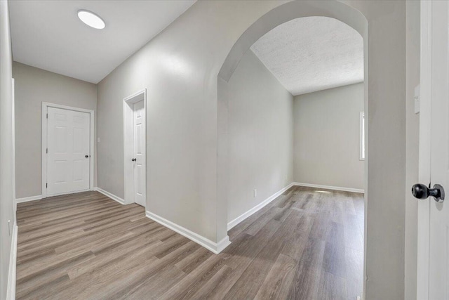 corridor featuring baseboards, arched walkways, a textured ceiling, and wood finished floors