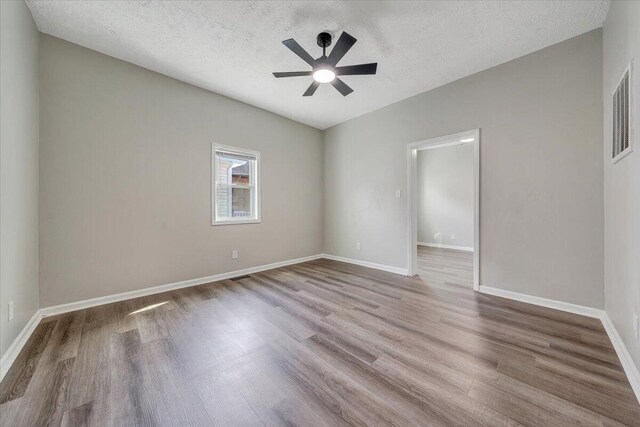 empty room with visible vents, a textured ceiling, wood finished floors, baseboards, and ceiling fan