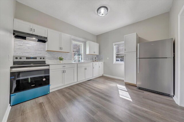 kitchen with under cabinet range hood, appliances with stainless steel finishes, white cabinets, light wood finished floors, and light countertops