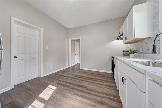 kitchen featuring wood finished floors, baseboards, a sink, white cabinets, and stainless steel range with electric stovetop