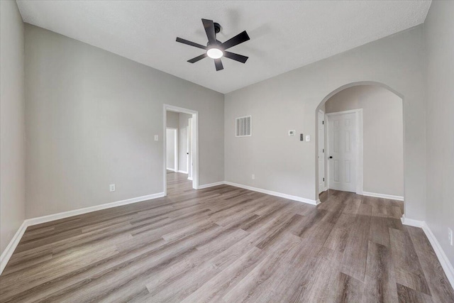 empty room featuring wood finished floors, arched walkways, visible vents, and baseboards