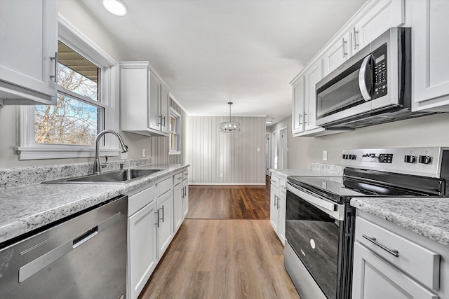 kitchen with a sink, wood finished floors, white cabinetry, stainless steel appliances, and light countertops