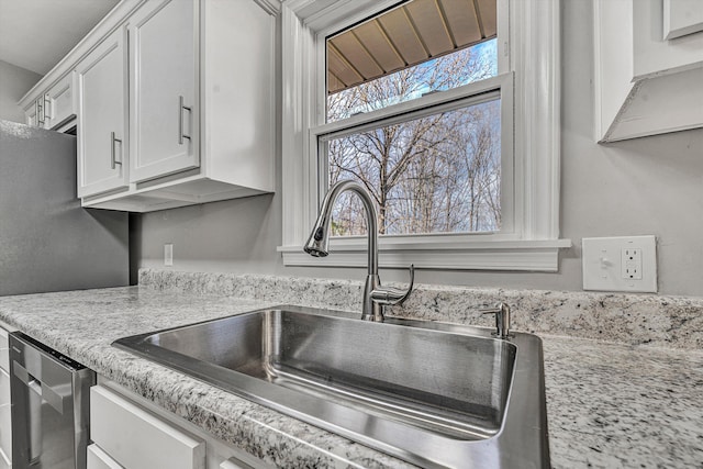 kitchen with white cabinetry, light stone counters, stainless steel dishwasher, and a sink