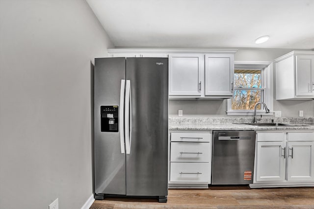 kitchen with baseboards, stainless steel appliances, wood finished floors, white cabinetry, and a sink