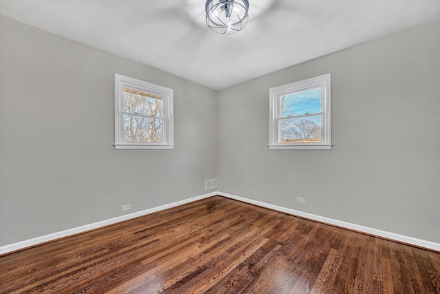 empty room with visible vents, a healthy amount of sunlight, dark wood-type flooring, and baseboards