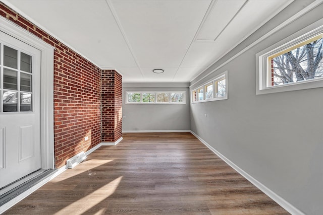 empty room featuring brick wall, baseboards, and wood finished floors