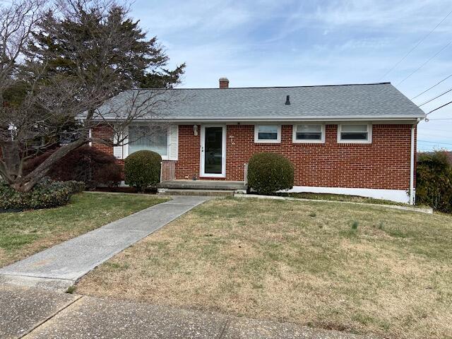 ranch-style home with a front lawn, brick siding, roof with shingles, and a chimney