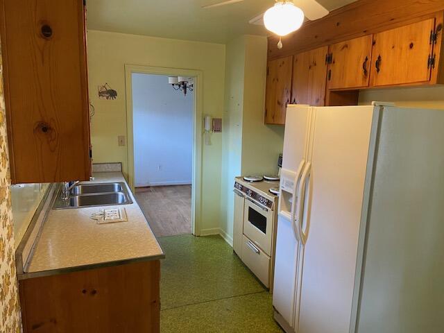 kitchen featuring brown cabinets, a ceiling fan, a sink, white appliances, and light countertops