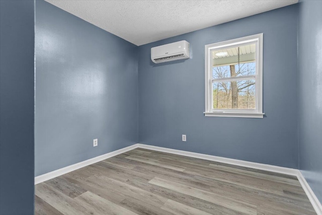 empty room featuring wood finished floors, baseboards, a wall mounted air conditioner, and a textured ceiling