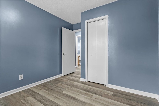 unfurnished bedroom with wood finished floors, baseboards, a closet, and a textured ceiling