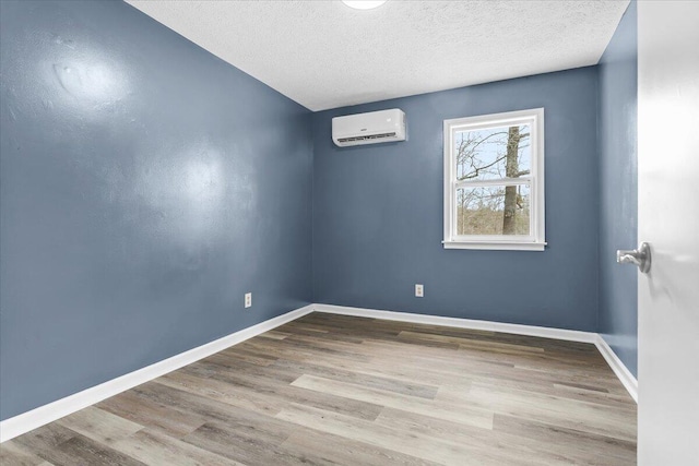 unfurnished room with a textured ceiling, wood finished floors, baseboards, and a wall mounted AC