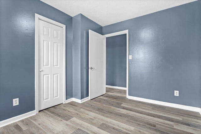 unfurnished bedroom featuring wood finished floors, baseboards, a closet, and a textured ceiling