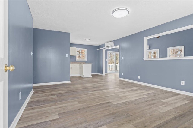 unfurnished living room with baseboards, wood finished floors, and a wall mounted AC