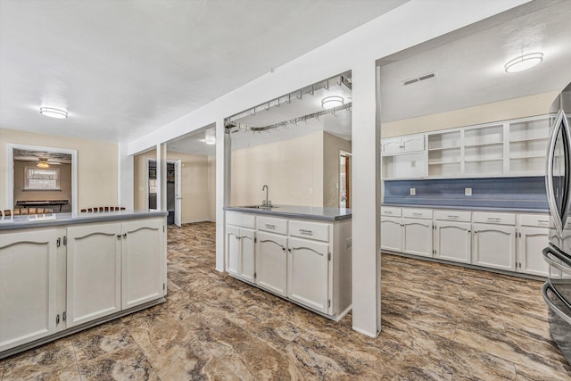 kitchen with dark countertops, visible vents, stainless steel refrigerator, a ceiling fan, and a sink