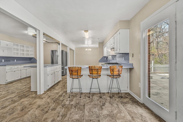 kitchen with a wealth of natural light, white cabinets, a peninsula, and freestanding refrigerator