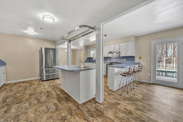 kitchen featuring a sink, under cabinet range hood, stainless steel appliances, a peninsula, and a breakfast bar area