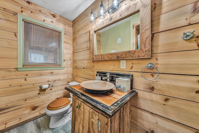 bathroom with vanity, wooden walls, toilet, and wood finished floors