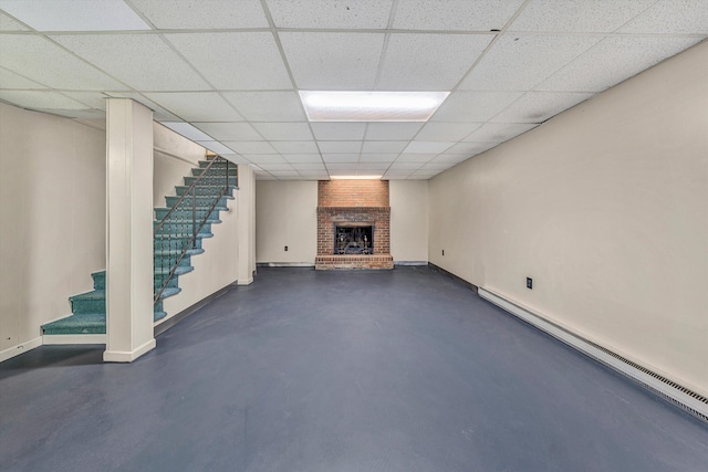 finished basement featuring baseboards, stairs, a fireplace, a paneled ceiling, and a baseboard radiator