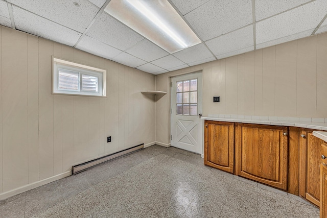 interior space featuring wooden walls, light floors, baseboards, a drop ceiling, and baseboard heating