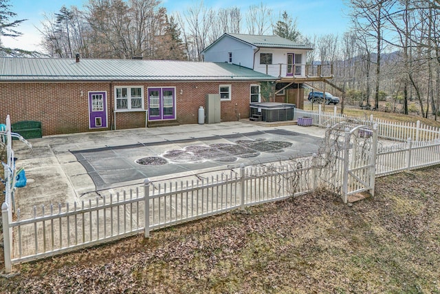 rear view of house featuring fence, a hot tub, a patio area, brick siding, and metal roof