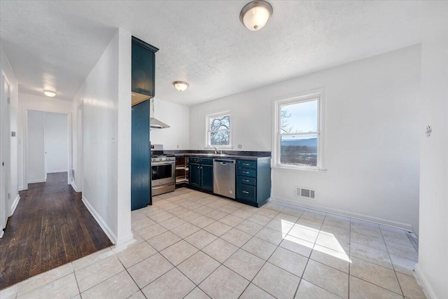 kitchen with blue cabinets, stainless steel appliances, a textured ceiling, and visible vents