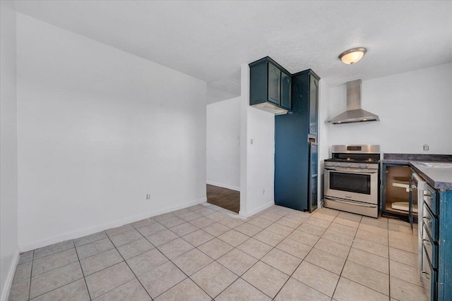 kitchen featuring stainless steel gas stove, dark countertops, wall chimney range hood, light tile patterned floors, and baseboards