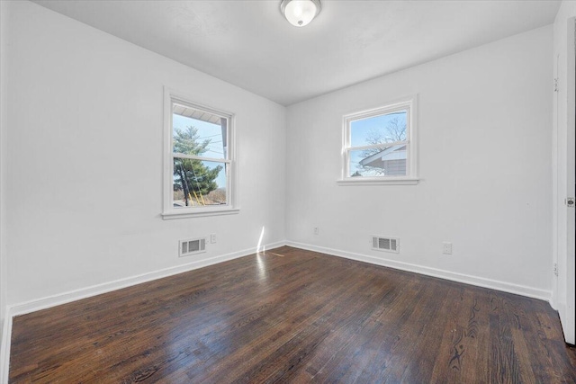 spare room featuring dark wood finished floors, visible vents, and a healthy amount of sunlight