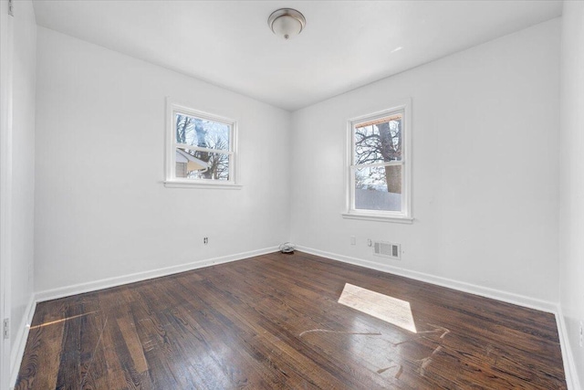 empty room featuring visible vents, baseboards, and dark wood-style flooring