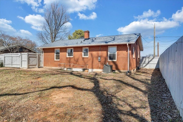 back of house featuring central air condition unit, a gate, fence, brick siding, and a chimney