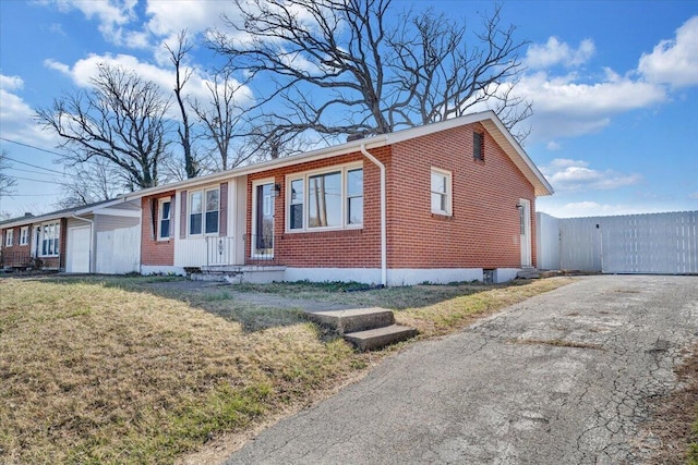 view of front facade featuring brick siding, fence, aphalt driveway, a front yard, and a gate