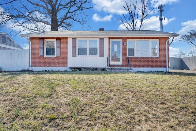 view of front facade with brick siding, a chimney, a front yard, and fence