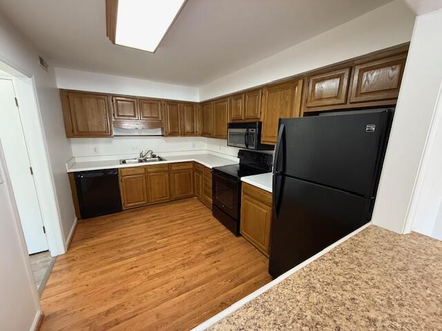 kitchen with black appliances, light wood-style flooring, light countertops, and a sink