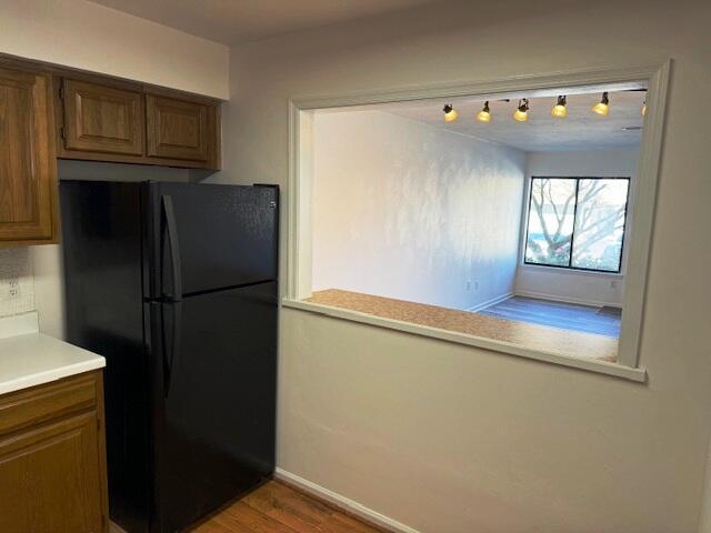 kitchen featuring brown cabinetry, wood finished floors, baseboards, freestanding refrigerator, and light countertops