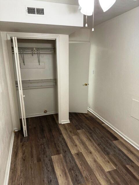 unfurnished bedroom with dark wood-style floors, visible vents, baseboards, ceiling fan, and a closet