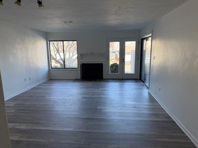 unfurnished living room with french doors, plenty of natural light, and dark wood-type flooring