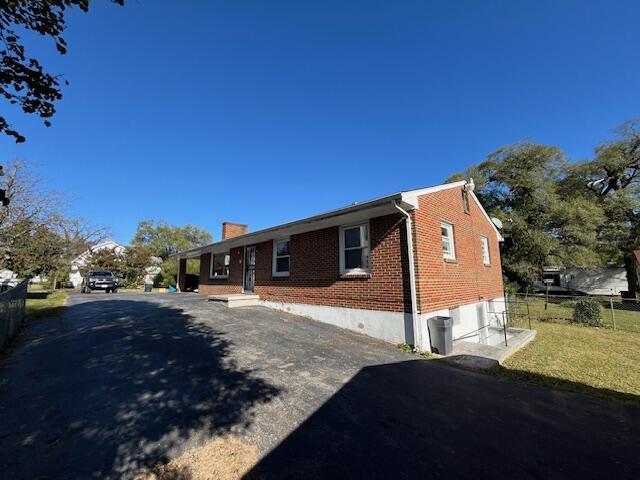 view of front facade with driveway, fence, a front yard, brick siding, and a chimney