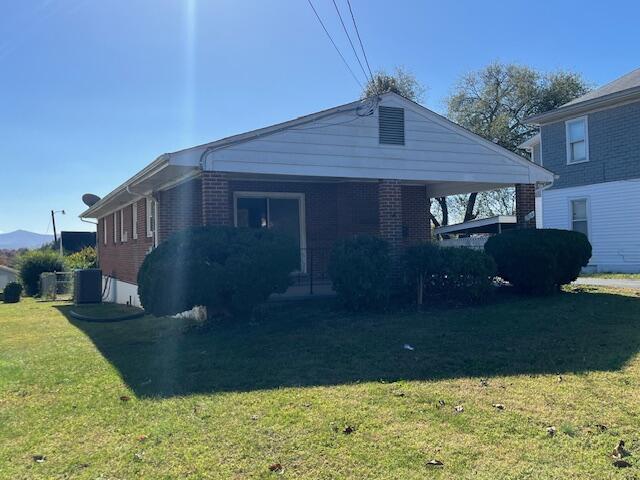 view of front of property with a front yard, central air condition unit, a carport, and brick siding