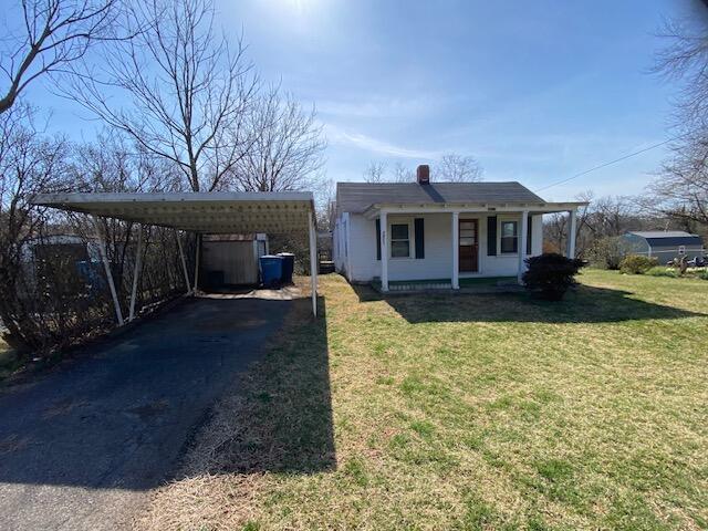 bungalow with aphalt driveway, covered porch, a detached carport, and a front yard