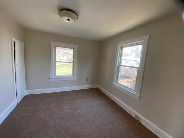 empty room with a wealth of natural light, baseboards, and dark carpet