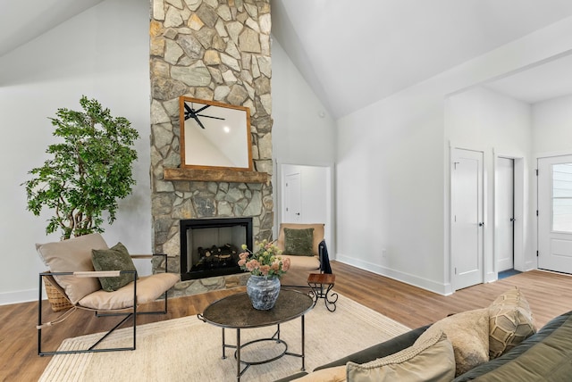 living area with a stone fireplace, high vaulted ceiling, baseboards, and wood finished floors