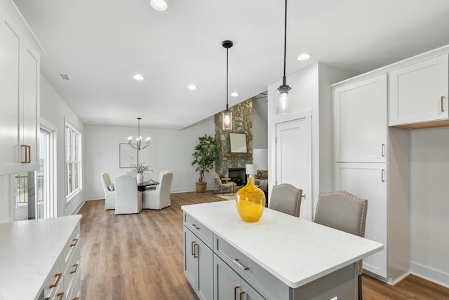 kitchen with light stone counters, wood finished floors, a center island, a stone fireplace, and white cabinets