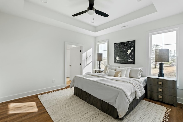 bedroom featuring a raised ceiling, visible vents, baseboards, and dark wood-type flooring