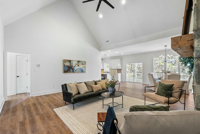 living room featuring ceiling fan with notable chandelier, high vaulted ceiling, baseboards, and wood finished floors