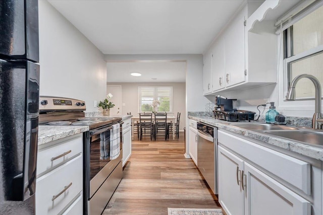 kitchen featuring light countertops, light wood-style flooring, white cabinets, stainless steel appliances, and a sink