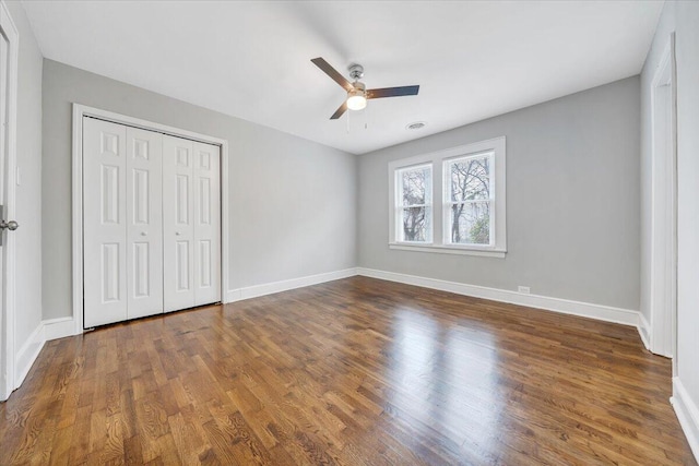 unfurnished bedroom with wood finished floors, baseboards, a closet, and ceiling fan